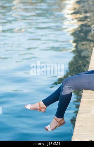 In prossimità di una donna per le gambe seduto sul pontile sul mare Foto Stock