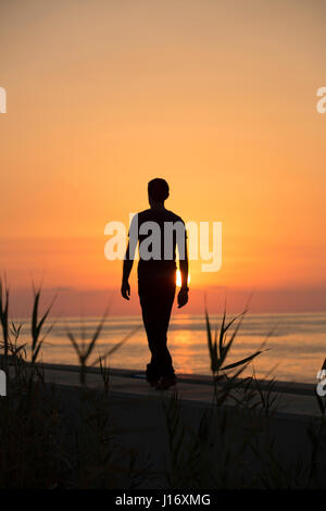 Lunghezza completa silhouette di una figura maschile di camminare sulla spiaggia al tramonto Foto Stock