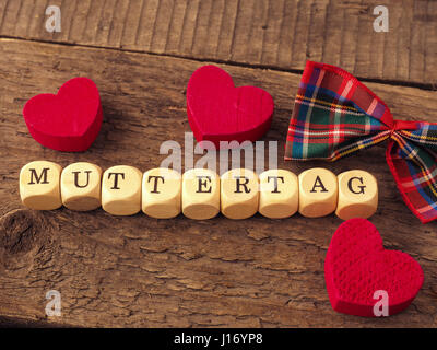 Festa della Mamma sfondo con la parola tedesca Mothersday su plinti in legno, cuore rosso forme e decorazioni di prua Foto Stock