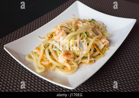 Delizioso cibo giapponese yaki Udon, Linguine con frutti di mare,shrips e verdura,piastra bianca su sfondi scuri. Foto Stock