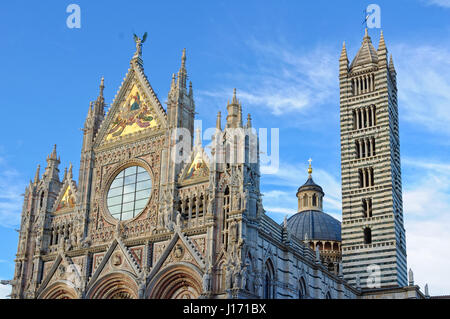 La facciata principale, il Duomo e la torre della cattedrale del Duomo di Siena sotto un paio di nuvole ed un cielo blu Foto Stock