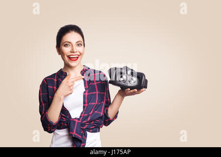 Giovane bella donna in stile casual con la realtà virtuale auricolare sullo sfondo beige. studio shot. Foto Stock