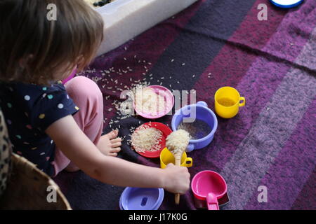 Close up della bambina gioca con il riso e il giocattolo piatti e tazze e cucchiai, gioco sensoriale Foto Stock