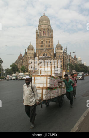 Gli uomini tirando il carrello caricato con pacchi di merci su strada in Mumbai, India Foto Stock