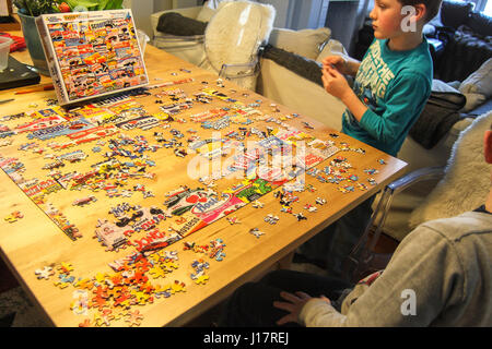 I bambini facendo puzzle. due giovani ragazzi lavorare su un parzialmente completata grande puzzle steso su una famiglia tavolo da pranzo. immagini di retro snack Foto Stock