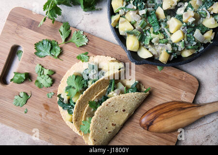 Due vegan soft tacos con ripieno di patate e spinaci e guarnita con il coriandolo su un tagliere con la padella di ferro di riempimento sul lato. Foto Stock