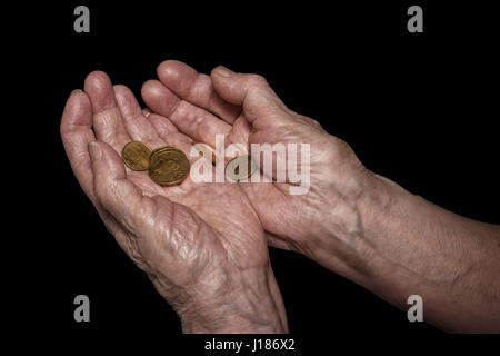 Senior donna mani tenendo alcune monete in euro. Pensione, la povertà, i problemi sociali e la senilità tema. Isolato su nero, percorso di clipping incluso Foto Stock