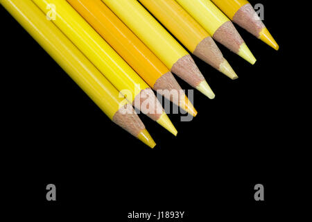 Sette matite di colore giallo tutti schierati in perfetta formazione angolato sulla pagina con un nero scuro dello sfondo. Foto Stock