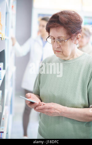 Donna matura utilizza lo smartphone in drug store Foto Stock