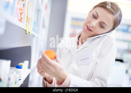 Il farmacista femmina su chiamata telefonica raggiungendo il farmaco Foto Stock