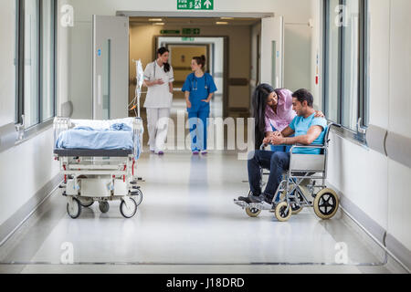 Maschio indiano asiatici paziente su sedia a rotelle con la moglie o fidanzata e infermieri in ospedale corridoio Foto Stock