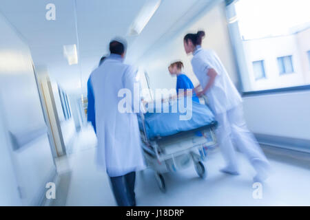 Un moto fotografia sfocata di un paziente sulla barella o barella essendo spinto in velocità attraverso un corridoio ospedaliero da parte di medici e infermieri in caso di emergenza Foto Stock