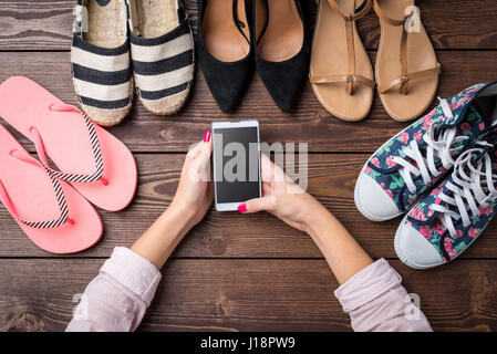Scarpe Donna collezione sul tavolo di legno con la donna con le mani in mano utilizzando smart phone Foto Stock