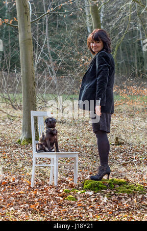 Una donna in abiti neri con un nero pug su una sedia bianca nella foresta Foto Stock