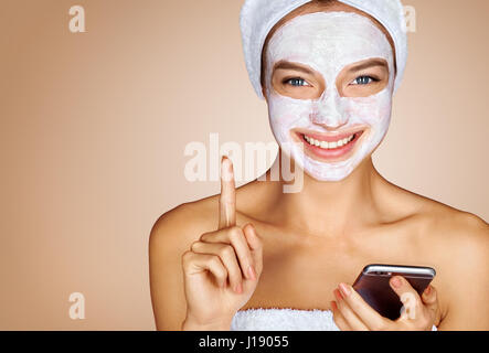 Funny Girl con maschera facciale utilizza lo smartphone. Foto di attraente giovane donna ricevere trattamenti spa. Beauty & Skin care concept Foto Stock