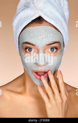 OMG! Bella ragazza con argilla maschera facciale. Foto della ragazza sorpreso con asciugamano sul suo capo su sfondo beige. Cura della Pelle concept Foto Stock