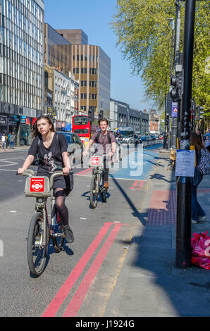 Un paio di ciclisti in sella Santander noleggiare biciclette giù Whitechapel High Street nella zona est di Londra. Foto Stock