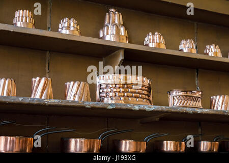 Raccolta di shiny vintage, antichi rame metallico jelly tumuli e altri utensili visualizzate allineate su un ripiano della tradizionale cucina passata ware Foto Stock