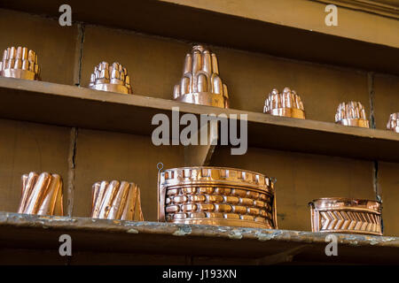 Raccolta di shiny vintage, antichi rame metallico jelly tumuli e altri utensili visualizzate allineate su un ripiano della tradizionale cucina passata ware Foto Stock