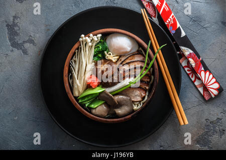 Spaghetti ramen con anatra, uovo, enoki e funghi shiitake con brodo su sfondo scuro Foto Stock