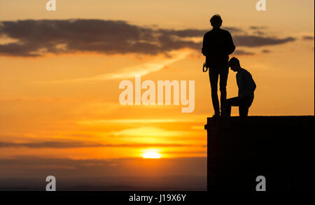 Silhouette di 2 amici in piedi su una parete in serata a guardare il sole andare giù. Foto Stock