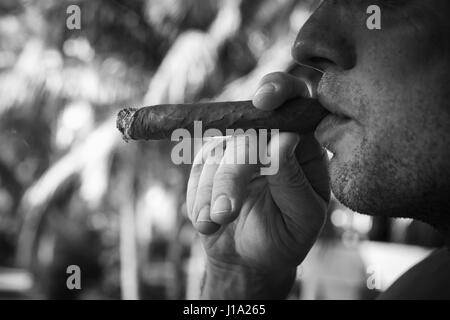 Giovane uomo europeo fuma grande sigaro, vicino la foto in bianco e nero con il fuoco selettivo. Repubblica Dominicana Foto Stock