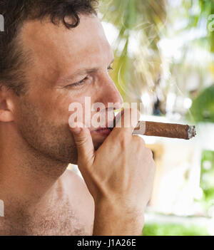 Giovane uomo europeo fuma grande sigaro, close up ritratto di profilo con il fuoco selettivo. Repubblica Dominicana Foto Stock