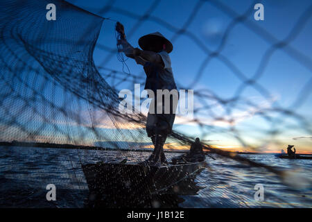 Thai pescatore sulla barca di legno di una rete di colata per la cattura di pesci di acqua dolce in natura fiume nelle prime ore della sera prima del tramonto Foto Stock