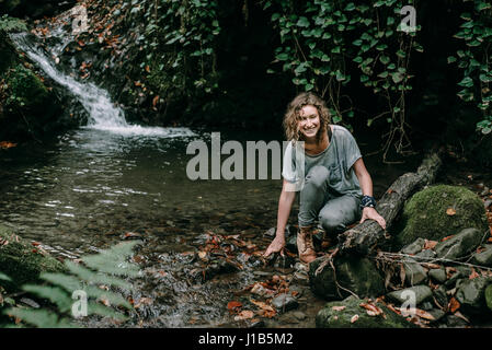 La donna caucasica accovacciato su roccia nel flusso della foresta Foto Stock