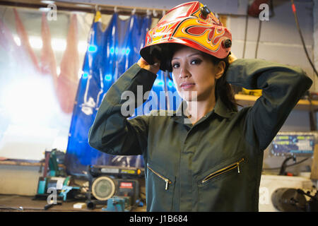 Razza mista donna che indossa la maschera protettiva in officina Foto Stock