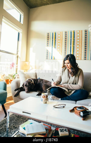 Razza mista donna sul divano con il cane iscritto nel journal Foto Stock