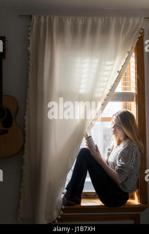 Donna sorridente seduta nella finestra utilizzando tavoletta digitale Foto Stock
