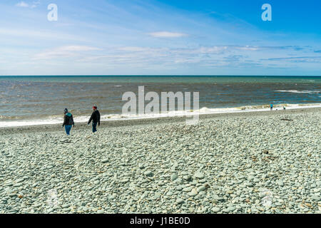 Un giovane uomo e donna camminando sulla spiaggia di ciottoli di Aberystwyth, Galles Foto Stock