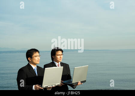 Due imprenditori che trasportano i loro notebook sulla spiaggia Foto Stock