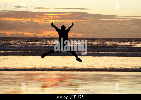 Un uomo salto sulla spiaggia che mostra la felicità (in silhouette) Foto Stock