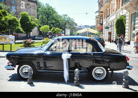 Lviv, Ucraina - 5 Giugno 2011: auto sovietica 60-xx anni Volga GAZ-21. Il driver attende coppia giovane è incoronato nella chiesa. Foto Stock