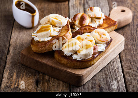 Colazione casalinga ricotta toast con banane a fettine e salsa di caramello servita su rustiche tagliere di legno Foto Stock