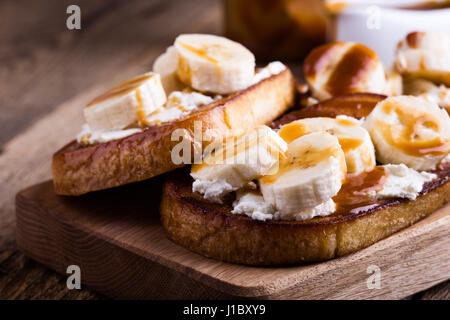 Colazione casalinga ricotta toast con banane a fettine e salsa di caramello servita su rustiche tagliere di legno Foto Stock
