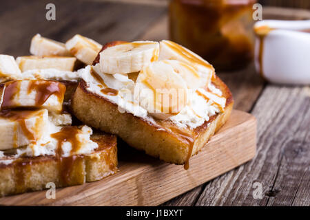 Colazione casalinga ricotta toast con banane a fettine e salsa di caramello servita su rustiche tagliere di legno Foto Stock