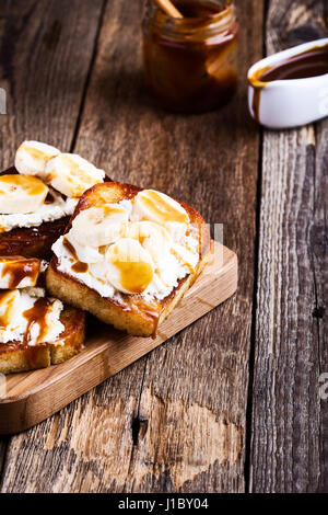 Colazione casalinga ricotta toast con banane a fettine e salsa di caramello servita su rustiche tagliere di legno Foto Stock