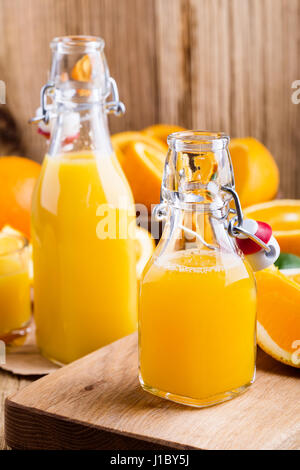 Spremuta di arancia fresca in bottiglie contro lo sfondo di agrumi freschi Foto Stock