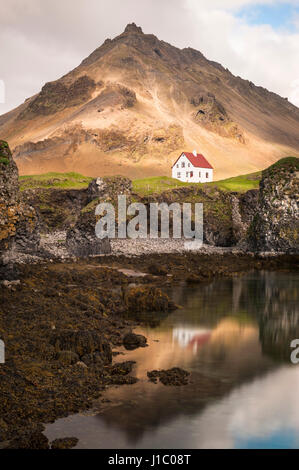 Arnarstapi, villaggio di pescatori islandese, casa isolata bianca sull'oceano sopra le rocce laviche, montagna Stapafell, penisola di Snæfellsnes, Islanda. Foto Stock