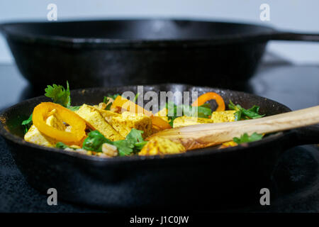 Vista laterale del cucchiaio di legno in agitazione il tofu, faro e verdure in padella in ghisa - cibo vegan concept Foto Stock