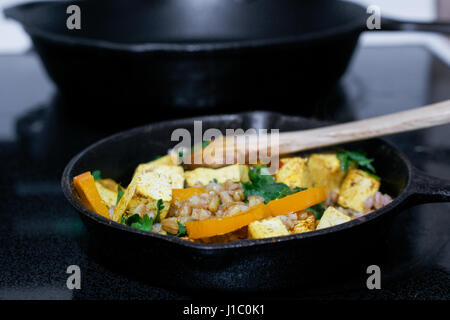 La cena angolo di visione di un cucchiaio di legno mescolando il tofu, faro e verdure in padella in ghisa - cibo vegan concept Foto Stock