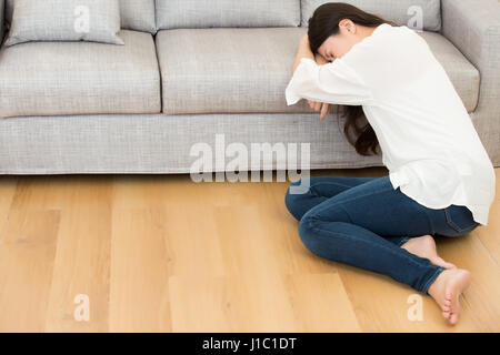 Giovane donna che soffre di mal di stomaco e il periodo dolore seduto sul piano casa. Lo stile di vita e il concetto di salute. razza mista asiatica modello cinese. Foto Stock