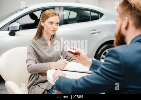 Barbuto venditore dando nuova chiave auto alla giovane donna carte di firma Foto Stock