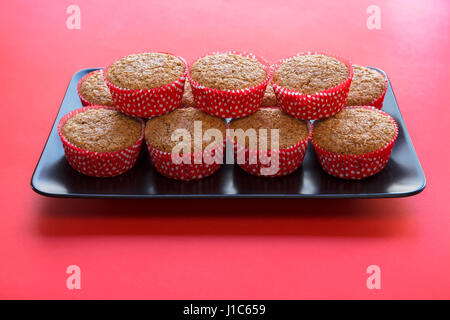 Bran muffin in rosso e bianco i titolari di carta su un nero piastra rettangolare e sfondo rosso Foto Stock