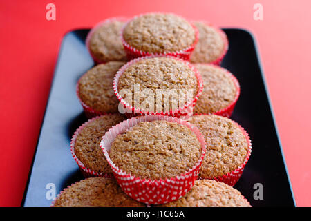 Bran muffin in rosso e bianco i titolari di carta su un nero piastra rettangolare e sfondo rosso Foto Stock