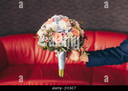 Uomo caucasico holding bouquet di fiori vicino al divano rosso Foto Stock