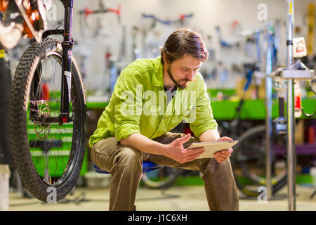 Lavoratore caucasica utilizzando digitale compressa nel negozio di biciclette Foto Stock